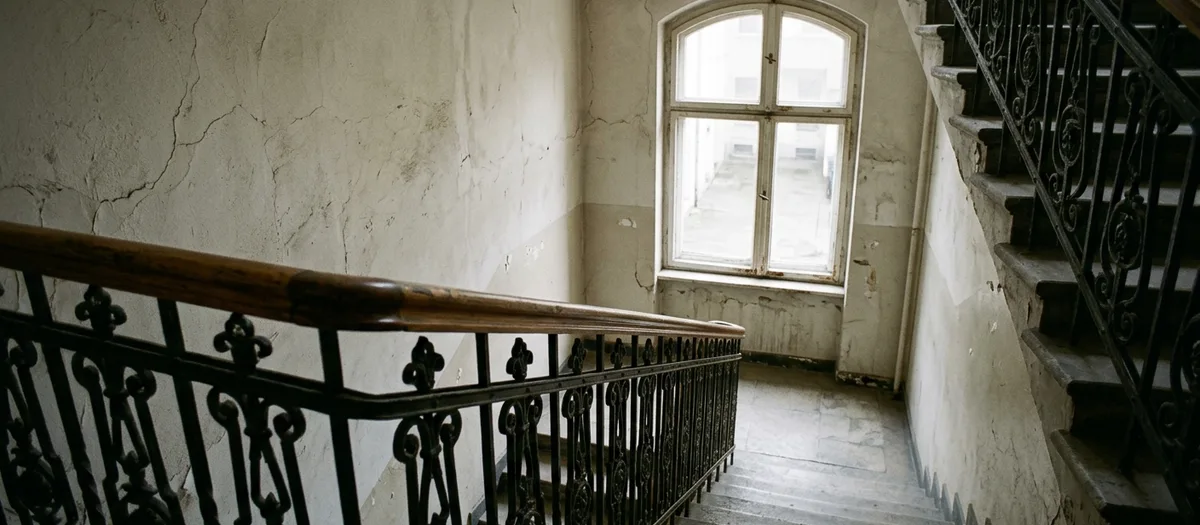 Treppenabsatz im Altbau mit schmiedeeisernem Geländer und Fenster zum Hof